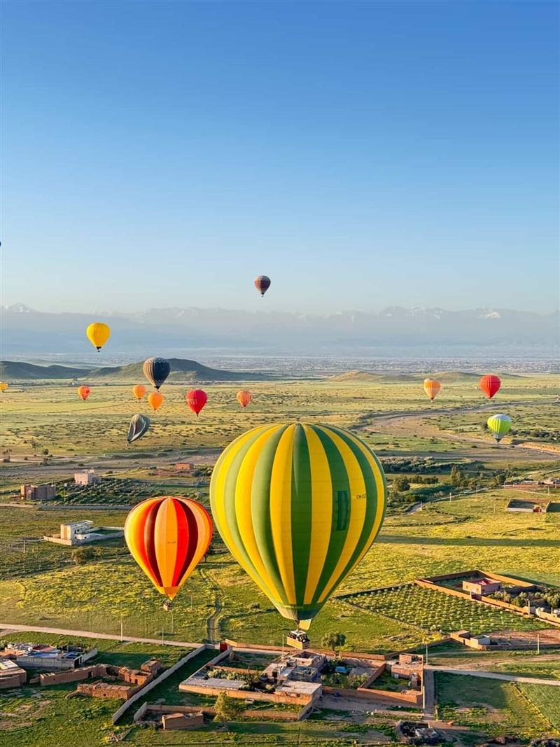 Striped balloons above green spring fields with snowy peaks behind