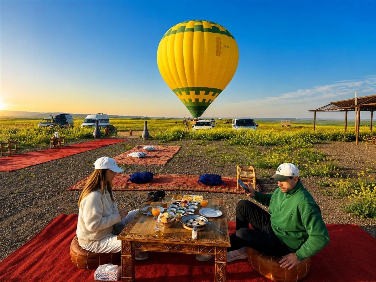 Couple having a private Moroccan breakfast on Berber rugs with a hot air balloon behind them near Marrakech