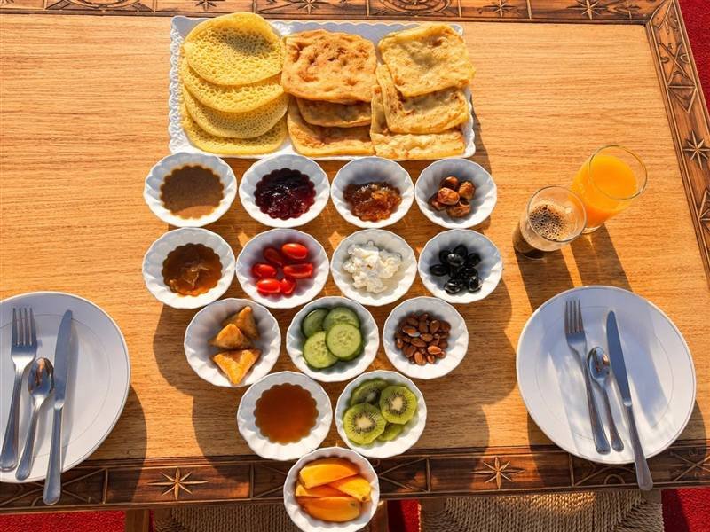 Traditional Moroccan breakfast on a private table: msemen, baghrir, honey, jams, dates, olives, fresh cheese, almonds, fruit, orange juice and coffee