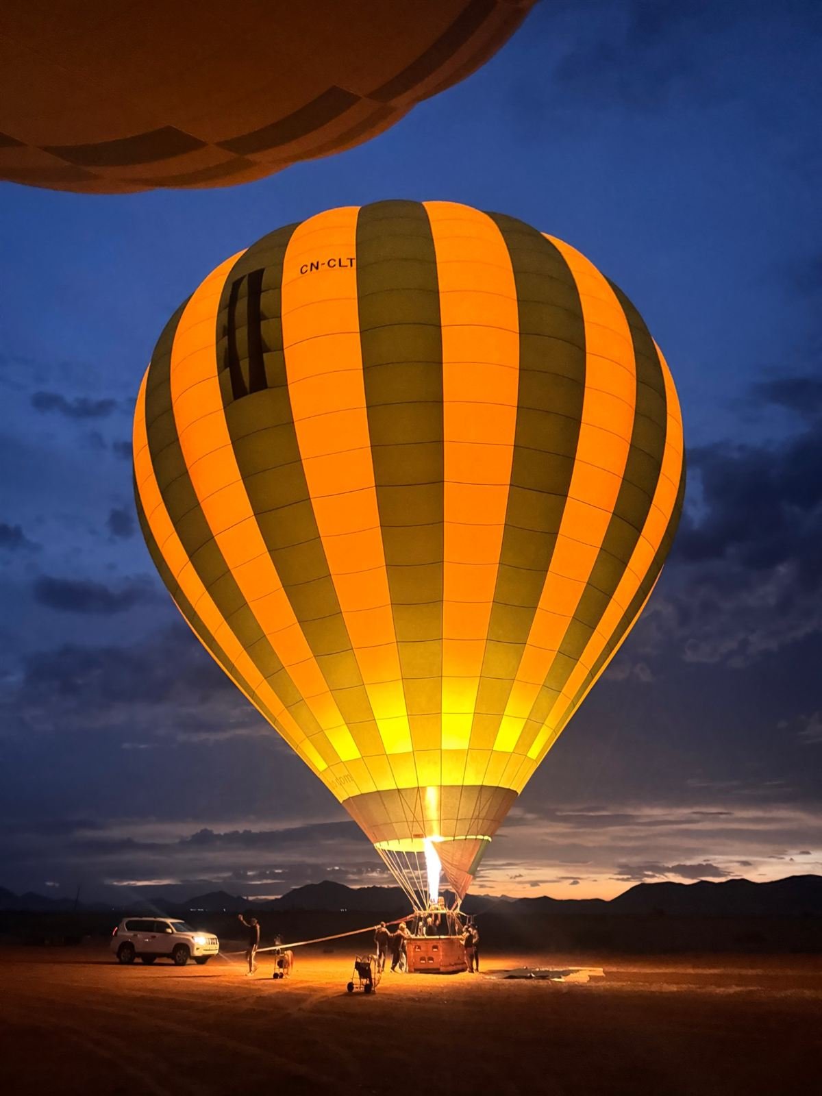 Balloon lit up by the burner under a deep blue sky before dawn