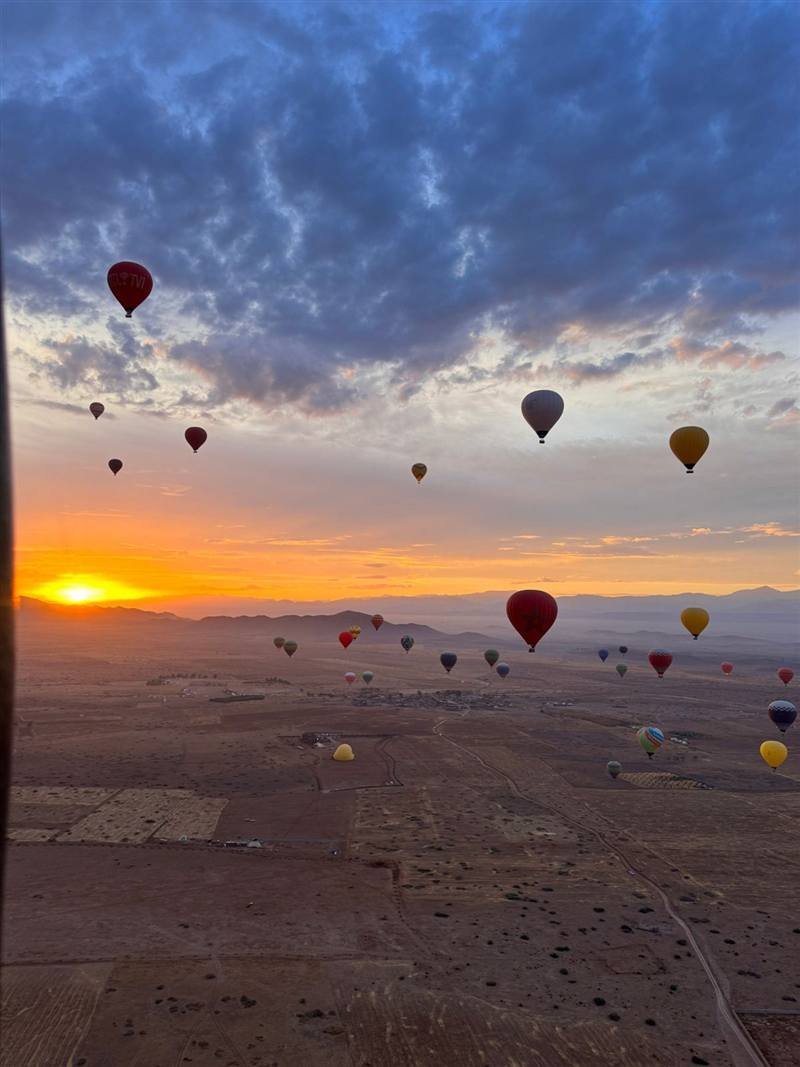 The sun rising behind the mountains with dozens of balloons in the sky